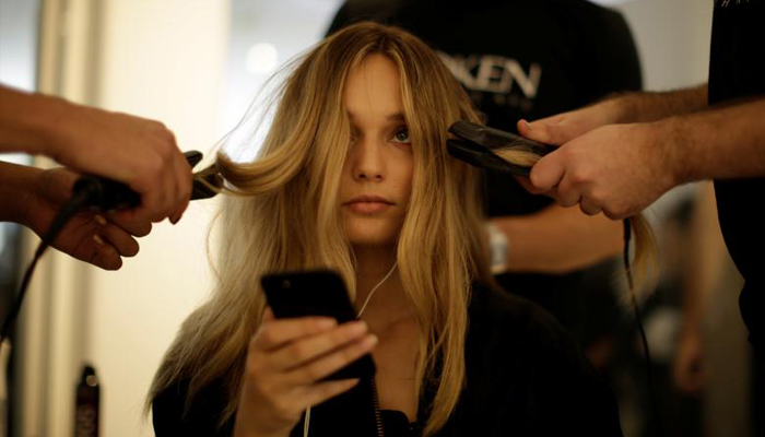 A model looks up from her mobile phone as stylists work on her hair before a show by Australian fashion house Albus Lumen. REUTERS/Jason Reed