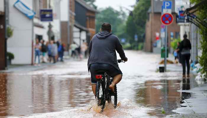 A cyclist drives through a flooded street following heavy rainfalls in Erftstadt, Germany, July 16, 2021. — Reuters/Thilo Schmuelgen