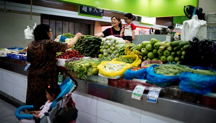 Two grandmothers with their granddaughter trade vegetables at a market on the outskirts of Shanghai, China June 3, 2021. Photo: Reuters