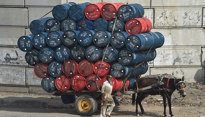 A man stands next to a horsecart laden with oil drums on a street in Lahore. Photo: AFP