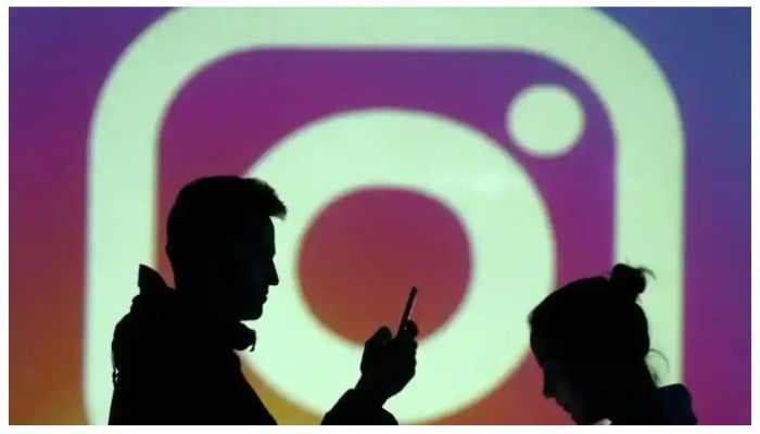 Silhouettes of mobile users are seen next to a screen projection of Instagram logo. Photo: Reuters