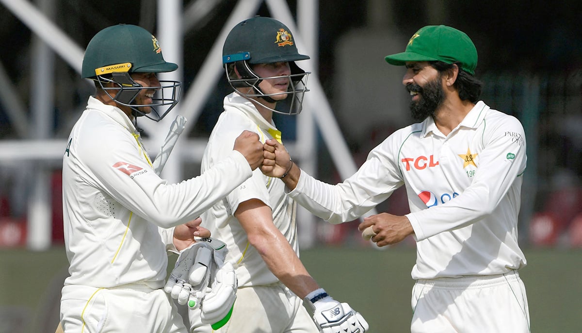 Pakistans Fawad Alam (R) congratulates Australias Usman Khawaja (L) after he scored a century (100 runs) as Australias Steve Smith watches during the fourth day of the third and final Test cricket match between Pakistan and Australia at the Gaddafi Cricket Stadium in Lahore on March 24, 2022. — AFP