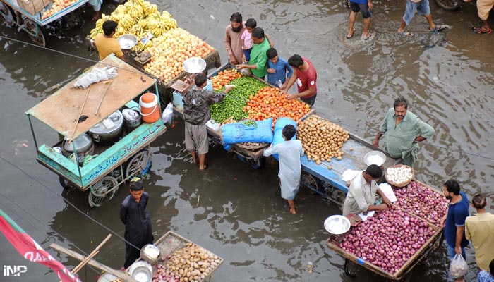 People buying vegetables from vendors who standing in flooded road at Unit 11 Latifabad after heavy rain in the city. — INP/File