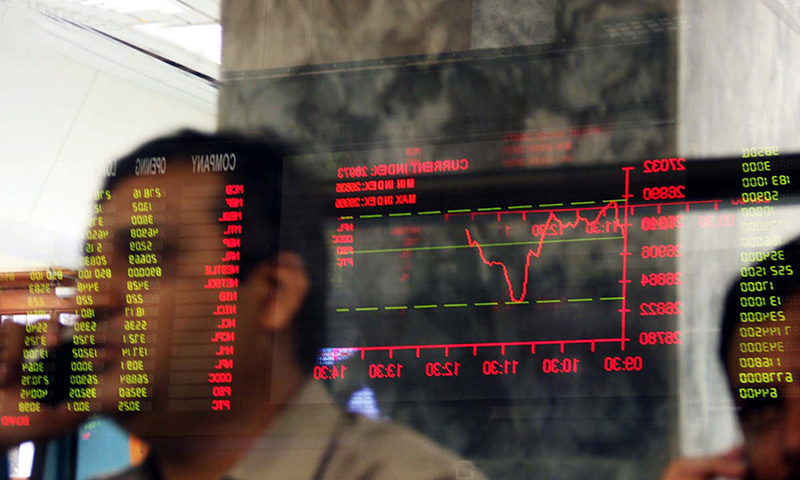 A stockbroker talks on a mobile phone as a trading screen is reflected on a glass pane at Pakistan Stock Exchange. — Reuters/File