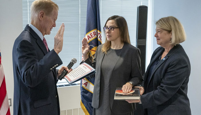 Dr Makenzie Lystrup (centre) holds up her right hand with her left hand placed on the book Pale Blue Dot, which is being held by Deputy Nasa Administrator Pam Melroy (right). Makenzie is looking at Nasa Administrator Bill Nelson who is also holding up his right hand and holding a piece of paper and a microphone in his left hand. — Twitter/@NASAGoddard