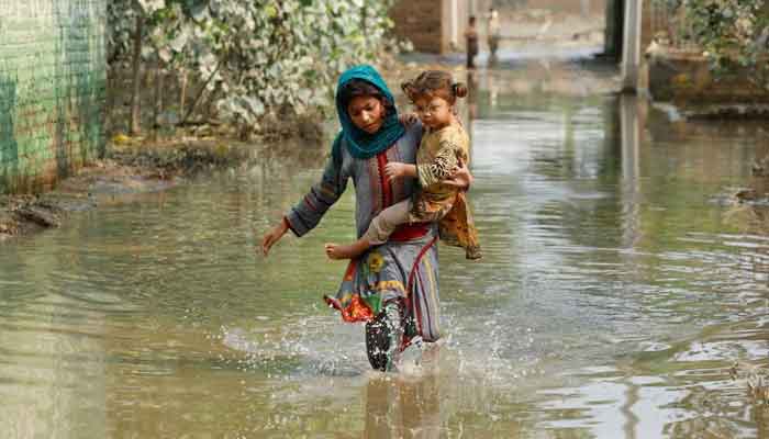 A girl carries her sibling as she walks through stranded flood water, following rains and floods during the monsoon season in Nowshera, Pakistan September 4, 2022.