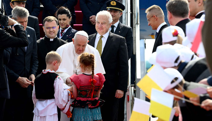 Hungarys deputy prime minister Zsolt Semjen (C-R) looks on as Pope Francis (C) is greeted by children wearing traditional Hungarian dresses after he arrived on April 28, 2023, at the Liszt Ferenc airport in Budapest. — AFP