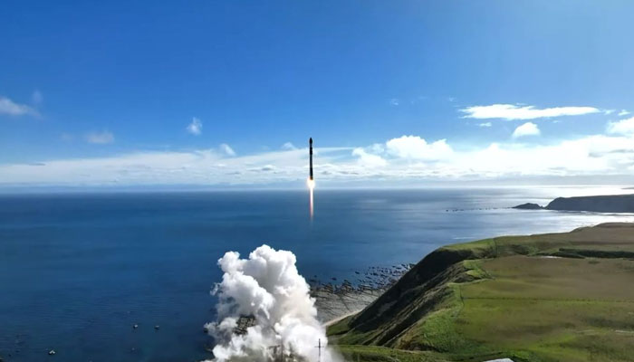 A black-and-white Rocket Lab Electron rocket lifts off from its launchpad in coastal New Zealand into a bright blue sky lined with bright, white clouds along the horizon on May 7, 2023. — Twitter/Nasa