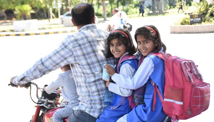 Student leave for their homes with their father on a bike after school timings end in Islamabad on May 10, 2023. — Online