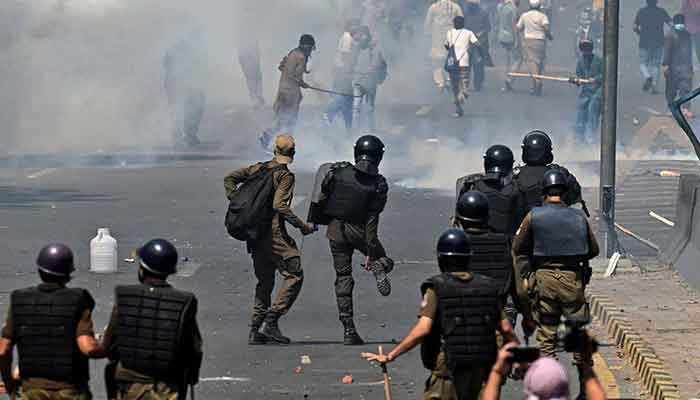 Police (foreground) use tear gas to disperse Pakistan Tehreek-e-Insaf activists and supporters of former prime minister Imran Khan during a protest against the arrest of their leader, in Lahore on May 10, 2023. — AFP