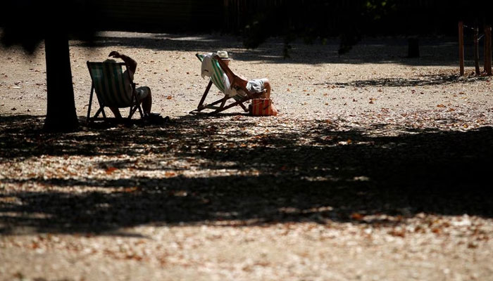 People sit in the sun, surrounded by parched grass during a period of hot and dry weather, in London, Britain, August 9, 2022. — Reuters