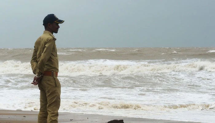 ایک پولیس اہلکار 15 جون، 2023 کو سمندری طوفان بِپرجوئے کے لینڈ فال سے پہلے، جاکھاؤ پورٹ کے تقریباً 100 کلومیٹر جنوب مشرق میں مانڈوی کے ساحل پر لہروں کے ٹکراتے ہوئے دیکھ رہا ہے۔  - اے ایف پی