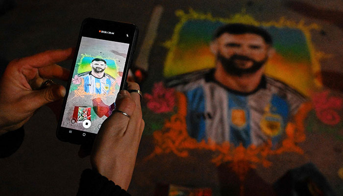 A woman takes a photo of a drawing by artist Claudio Papillon depicting Argentine football star Lionel Messi, at 9 de Julio Avenue in Buenos Aires, on June 19, 2023.—AFP