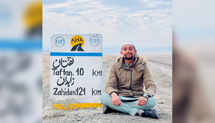 A Pakistani student, Usman Arshad takes rest next to a road sign of Taftan and Zahidan regions of Quetta Pakistan, in this handout photo obtained by Reuters on June 23, 2023. — Reuters