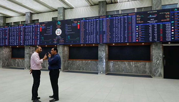 Men talk as they stand in front of electronic board displaying share market prices during a trading session in the hall of PSX in Karachi. — Reuters/File