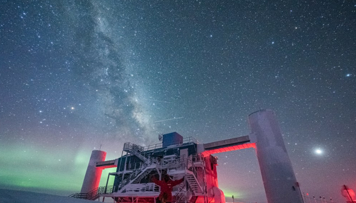 A winterover standing in front of the IceCube Lab at the South Pole, with auroras and Milky Way overhead in this picture released on June 29, 2023. — The IceCube Neutrino Observatory/NSF