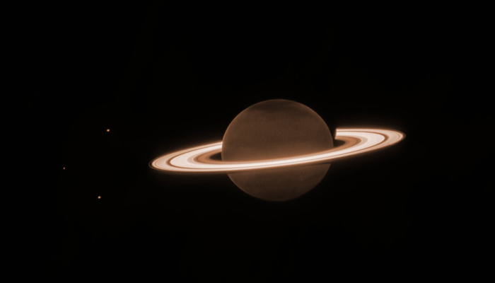 This image shows background dots of Saturns moon and at the centre is a dark orange-brown circle, surrounded by several blazing bright, thick, horizontal whiteish rings. This is Saturn and its rings. — Twitter/NasaWebb