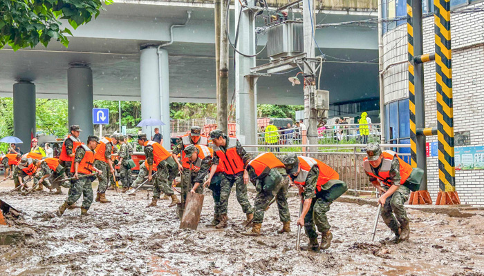 Paramilitary policemen clear a street after flooding caused by heavy rains in Chongqing. — AFP