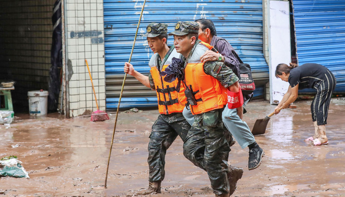 Paramilitary policemen evacuate a resident after flooding caused by heavy rains in Chongqing. — AFP