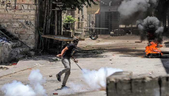 A masked Palestinian protester throws stones during clashes with Israeli forces in the centre of Hebron in the occupied West Bank on July 4, 2023. — AFP