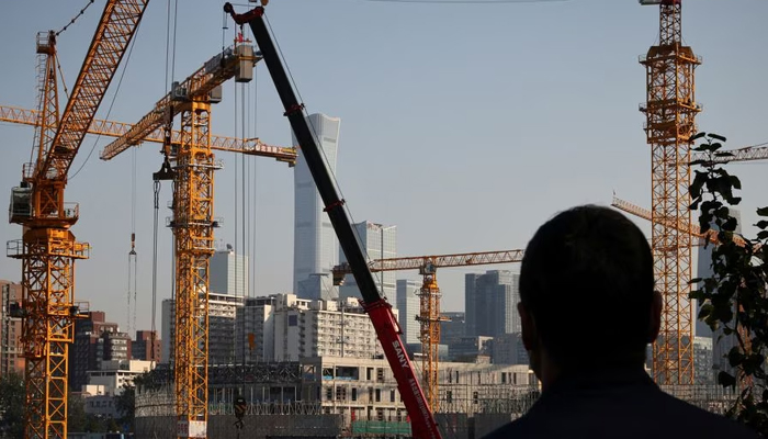 A person looks towards cranes in front of the skyline of the Central Business District (CBD) in Beijing, China, October 18, 2021. — Reuters