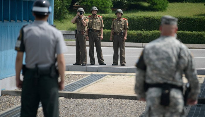 North Korean soldiers (C) take photos of a South Korean soldier (L) and a US soldier (R) standing before the military demarcation line (lower C) separating North and South Korea within the Joint Security Area (JSA) at Panmunjom. — AFP/File