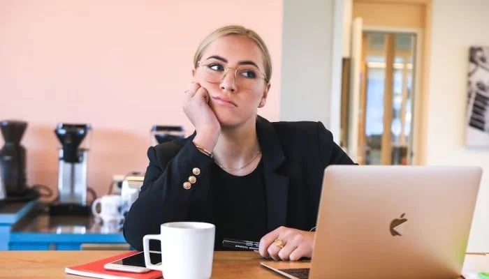 A woman sitting in front of her MacBook, looking away.— Unsplash