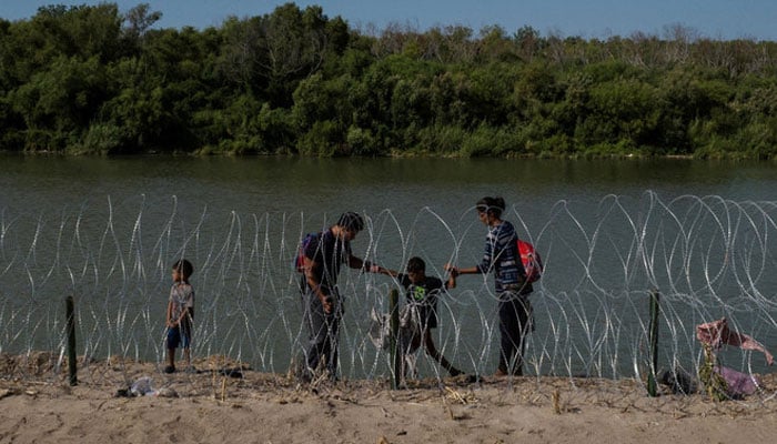 A family navigates the bank of the Rio Grande past razor wire while searching for an entry point into the United States from Mexico, in Eagle Pass, Texas, US, July 30, 2023. (Reuters)