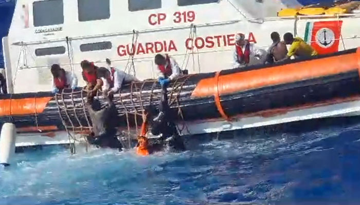 This handout photograph taken on August 5, 2023 by Italian Coastguard (Guardia Costeria) and released on August 6, 2023, shows rescuers helping migrants to board a rescue boat during operations that took place south of Lampedusa, rescuing 57 migrants and also recovering the lifeless bodies of a woman and a minor on board. — AFP