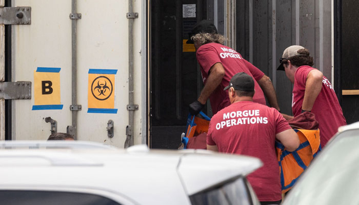 Workers wearing Morgue Operations shirts move a body bag into a refrigerated storage container adjacent to the Maui Police Forensic Facility where human remains are stored in the aftermath of the Maui wildfires in Wailuku, Hawaii on August 15, 2023. — AFP