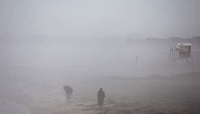 People walk in the rain along the Pacific Ocean with Tropical Storm Hilary approaching in San Diego County on August 20, 2023, in Imperial Beach, California. — AFP