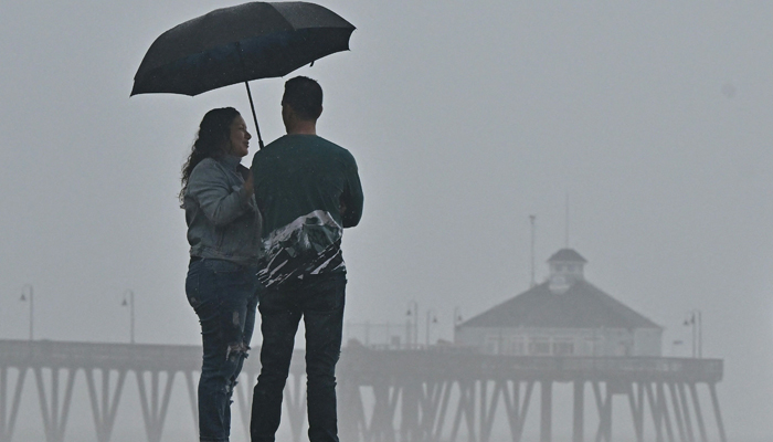 A couple shares an umbrella while viewing the increasingly large waves hitting the southern California coast, ahead of Tropical Storm Hilary in Imperial Beach, California, on August 20, 2023. — AFP