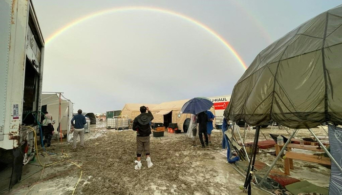 Attendees look at a rainbow over flooding on a desert plain on September 1, 2023, after heavy rains turned the annual Burning Man festival site in Nevadas Black Rock desert into a mud pit. — AFP