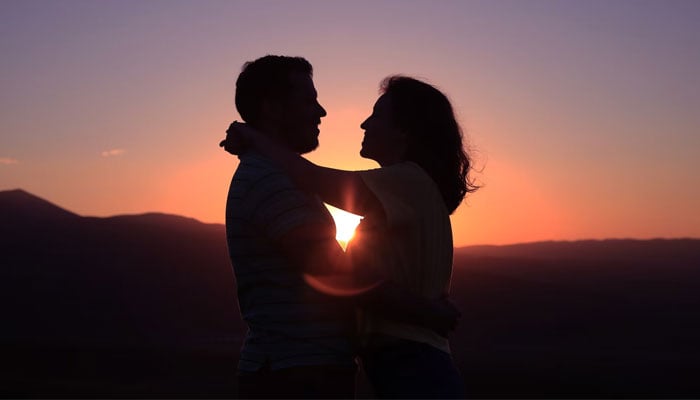 A couple with their arms wrapped around each other against a sunset view. — Unsplash/File