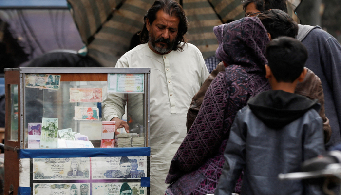 A currency broker stands near his booth, which is decorated with pictures of currency notes, while dealing with customers, along a road in Karachi, January 27, 2023. — Reuters