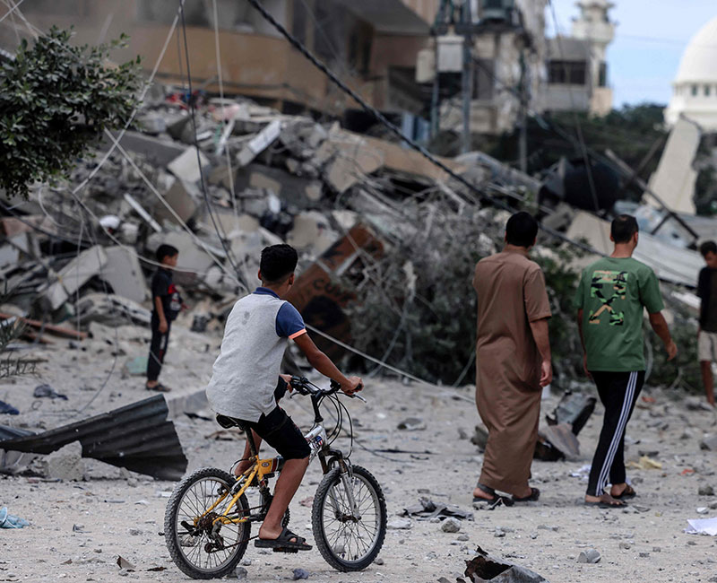 A young man rides his bicycle past a building destroyed by Israeli air strikes in Gaza City on October 7, 2023. — AFP