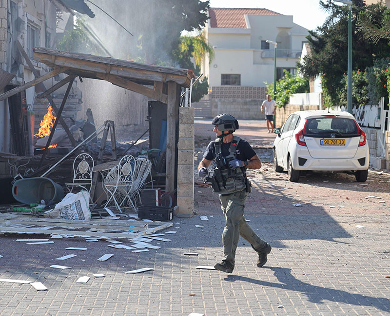 A member of the Israeli forces runs past a fire rages in a house in Ashkelon, following a rocket attack from the Gaza Strip on southern Israel on October 7, 2023. — AFP