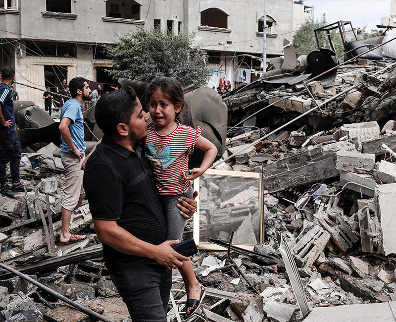 A man carries a crying child as he walks in front of a building destroyed in an Israeli air strike in Gaza City on October 7, 2023. — AFP