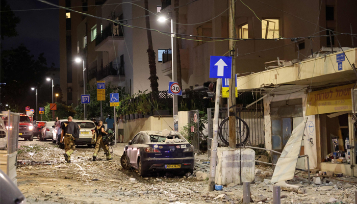 Members of the occupied Israeli security forces walk along a debris-strewn street in Tel Aviv, after it was hit by a rocket fired from the Gaza Strip on October 7, 2023. — AFP
