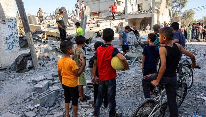 Children watch as civil defence responders search for victims in the rubble of a building after an Israeli air strike in Rafah in the southern Gaza Strip on October 13, 2023. — AFP