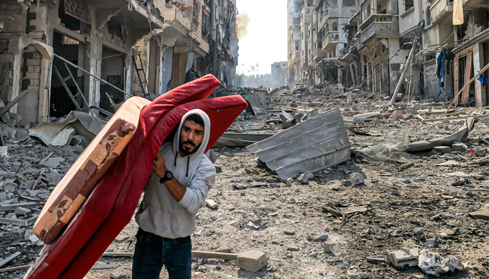 A man walks with mattresses through destruction in the Gaza Strip´s Jabalia refugee camp on October 11, 2023, following overnight Israeli airstrikes. — AFP