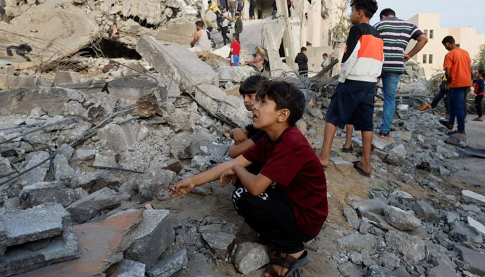 Palestinian children sit amid the rubble as others search a building destroyed by Israeli air raids in Khan Younis in the southern Gaza Strip [Mohammed Salem/Reuters