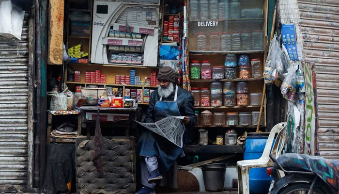 A man reads newspaper while selling betel leaves, known as pan, cigarettes and candies from a shop in Karachi, Pakistan, December 30, 2021. — Reuters