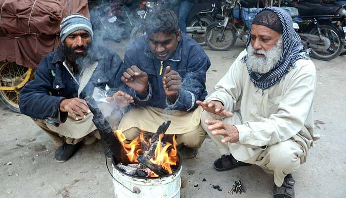 People sitting around wooden fire to keep them warm during chilled weather in city. — APP