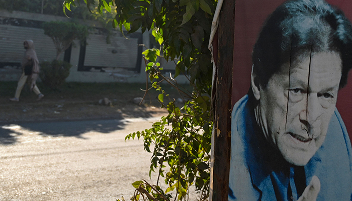 A woman walks past a poster of former prime minister Imran Khan near his Banigala residence, in Islamabad on December 23, 2023. — AFP