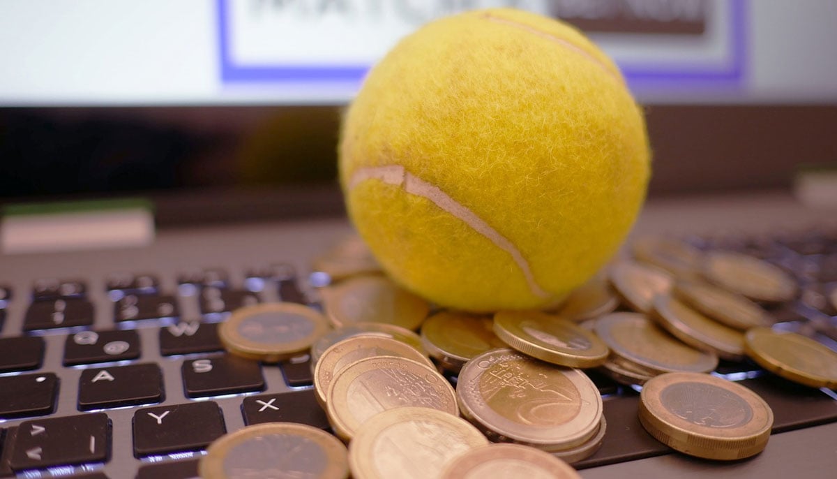 A representational image of a tennis ball kept on coins and a laptop. — Pixabay