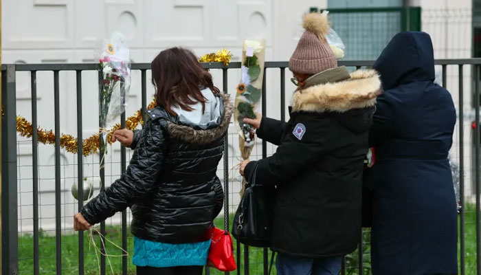 People lay flowers in front of the ground floor flat where the bodies of a woman and her four children where discovered, in Meaux, east of Paris, on December 26, 2023.—AFP