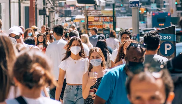 A representational image showing people in masks crossing a crowded street. — Unsplash