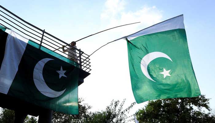 A boy uses a bamboo stick to adjust national flags at an overhead bridge ahead of Pakistans Independence Day, in Islamabad, Pakistan August 10, 2018. — Reuters