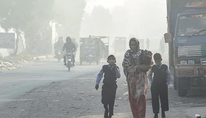 Children walk to school along a road amid smoggy conditions in Lahore in this undated image. — AFP